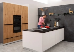 Moderne Küche mit Kücheninsel mit weißem Korpus und schwarzer Arbeitsplatte mit kleinem Tresen. Im Kontrast dazu Schränke aus Holz mit schwarzen Griffen.