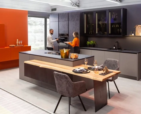 Moderne Küche in grau mit schwarzen Arbeitsplatten, schwarzen Armaturen mit Kücheninsel und niedrigem Tresen mit Essplatz. Als Kontrast dazu orange Wand mit gleichfarbigem Sideboard.